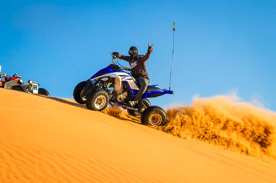 A quad throwing a wall of sand on a desert dune